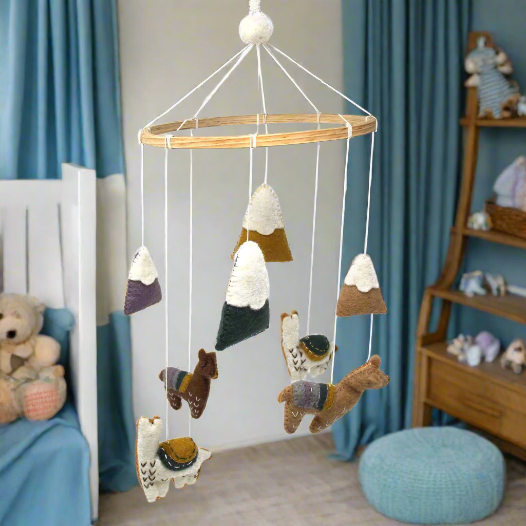 boys room in blue with hand-felted baby mobile hanging from a bamboo hoop. Mobile has four felt baby llamas and four felt snow capped mountains. fair trade product created by female artisans in Nepal and fair trade imported to the US.